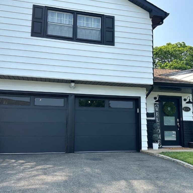 Two black modern garage doors installed on a white clapboard home