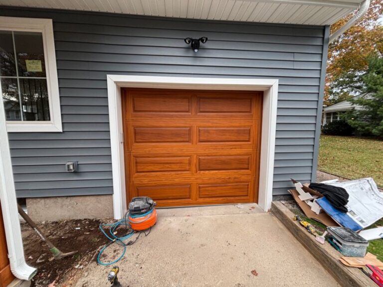 Oak-finish single garage door fitted to a grey clapboard home